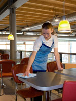 Professionelle Reinigungskraft reinigt Tisch in einer Cafeteria